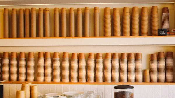 Paper cups stacked on shelves above an espresso machine in a café